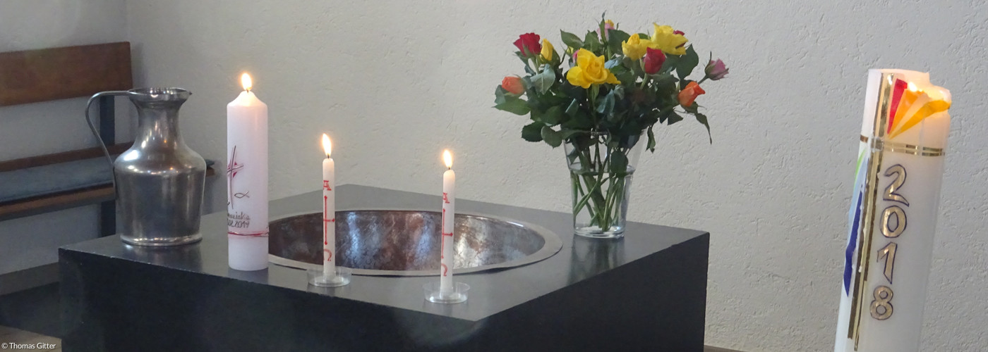 Taufstein mit brennenden Kerzen und Blumenstrauß