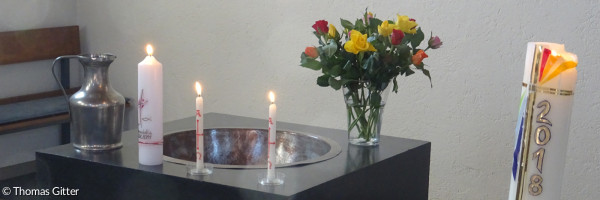 Taufstein mit brennenden Kerzen und Blumenstrauß