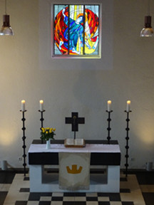 Altar mit Kerzen und über dem Altar ein buntes Kirchenfenster